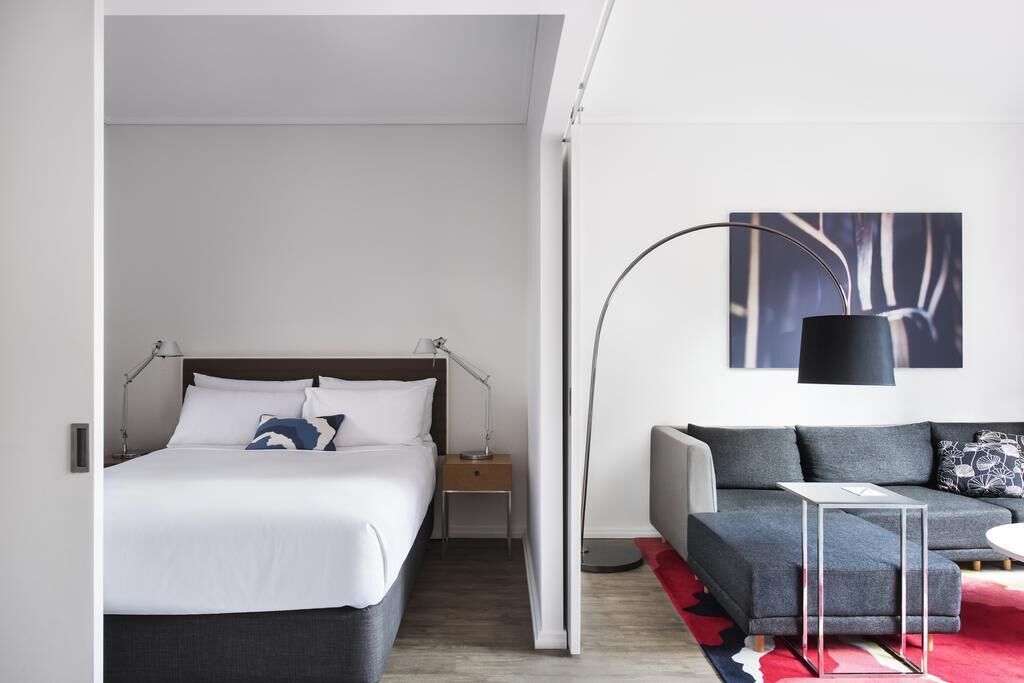 Ett modernt hotellrum med en säng, en soffa, ett litet bord och en golvlampa.