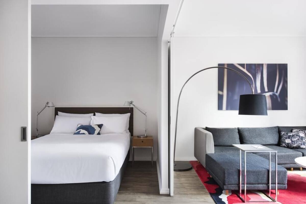 Ett modernt hotellrum med en säng, en soffa, ett litet bord och en golvlampa.