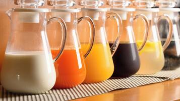 Une rangée de carafes en verre munies d’anses, chacune contenant un liquide de couleur différente, est placée sur un tapis tissé.