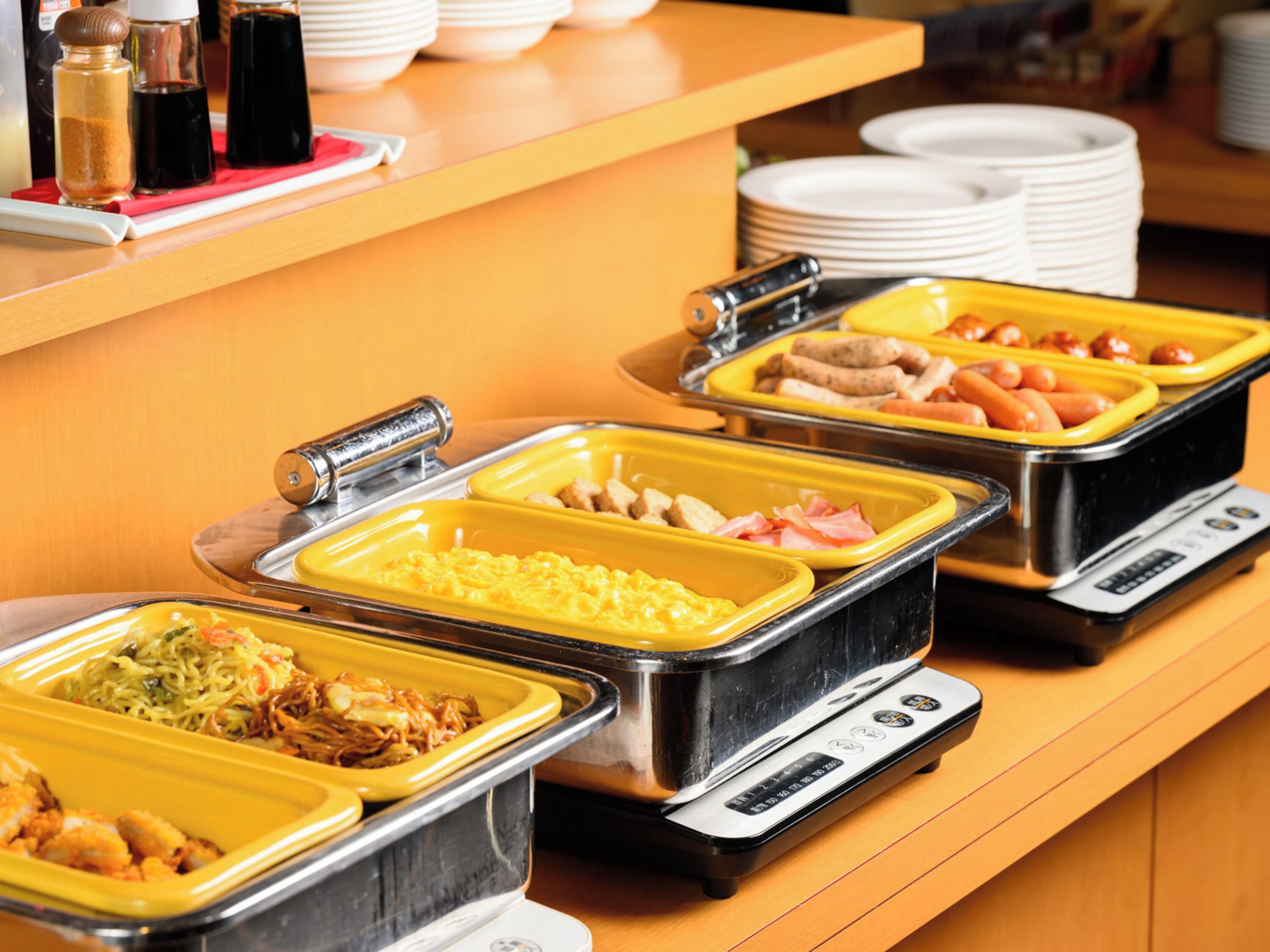 Un buffet proposant une variété de plats dans des récipients jaunes et noirs, notamment des nouilles, des œufs et de la viande.