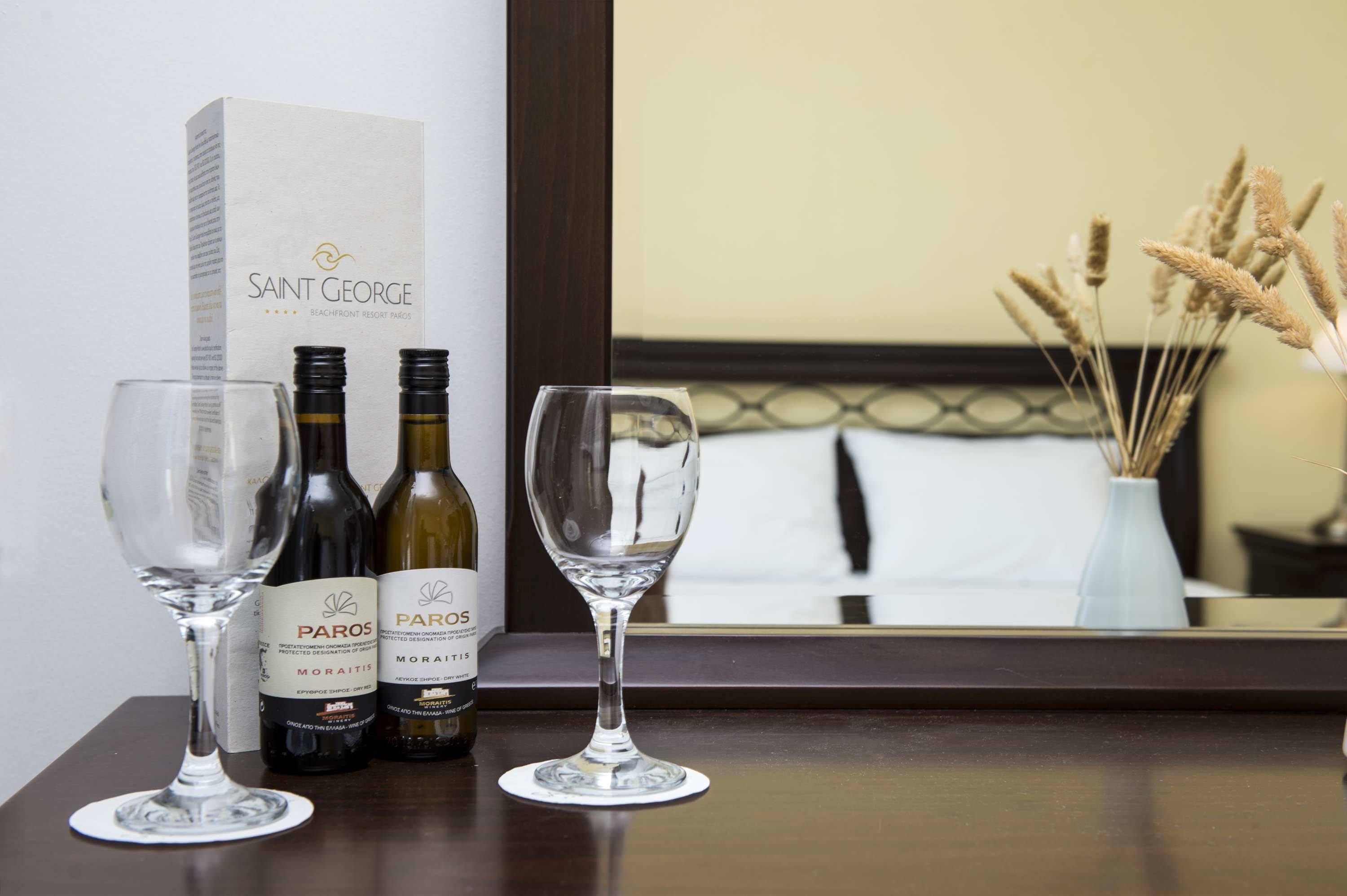 A hotel room with a wooden table displaying two wine bottles and two wine glasses. A box labeled "SAINT GEORGE" is also visible.