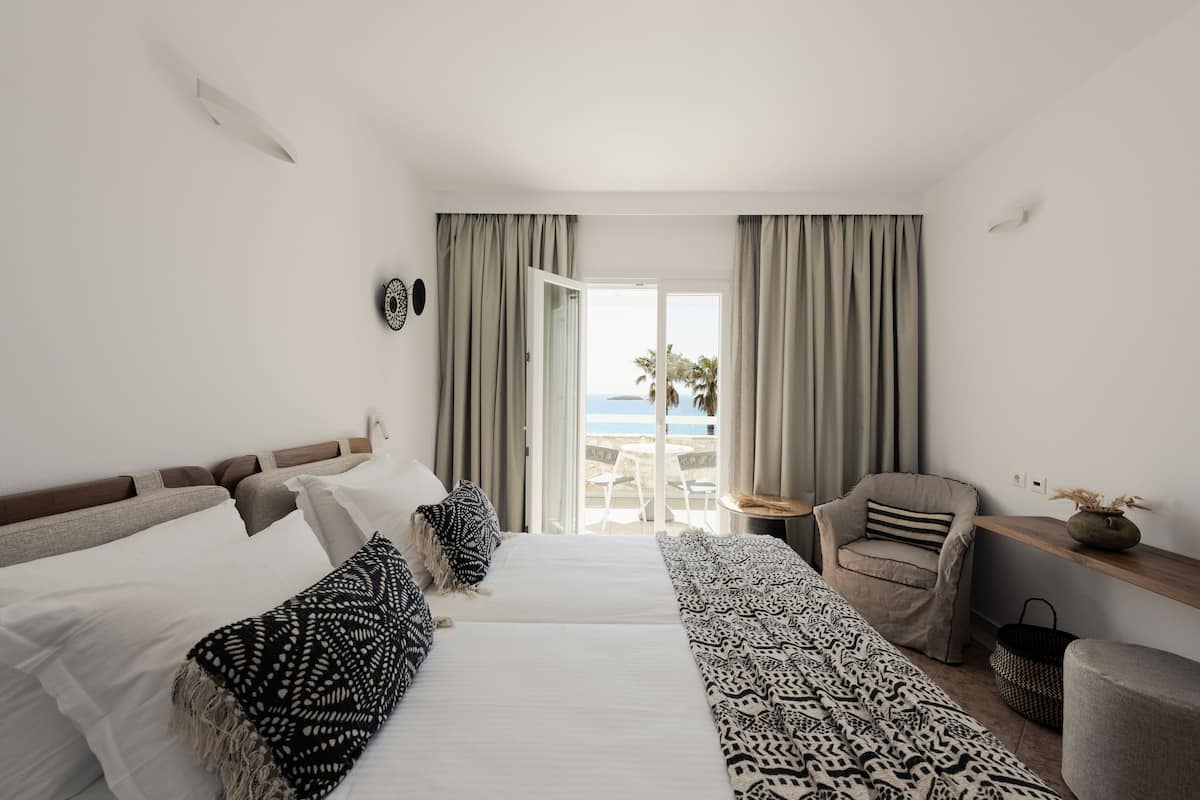 A hotel room with a bed, a chair, a small table, and a view of the beach.