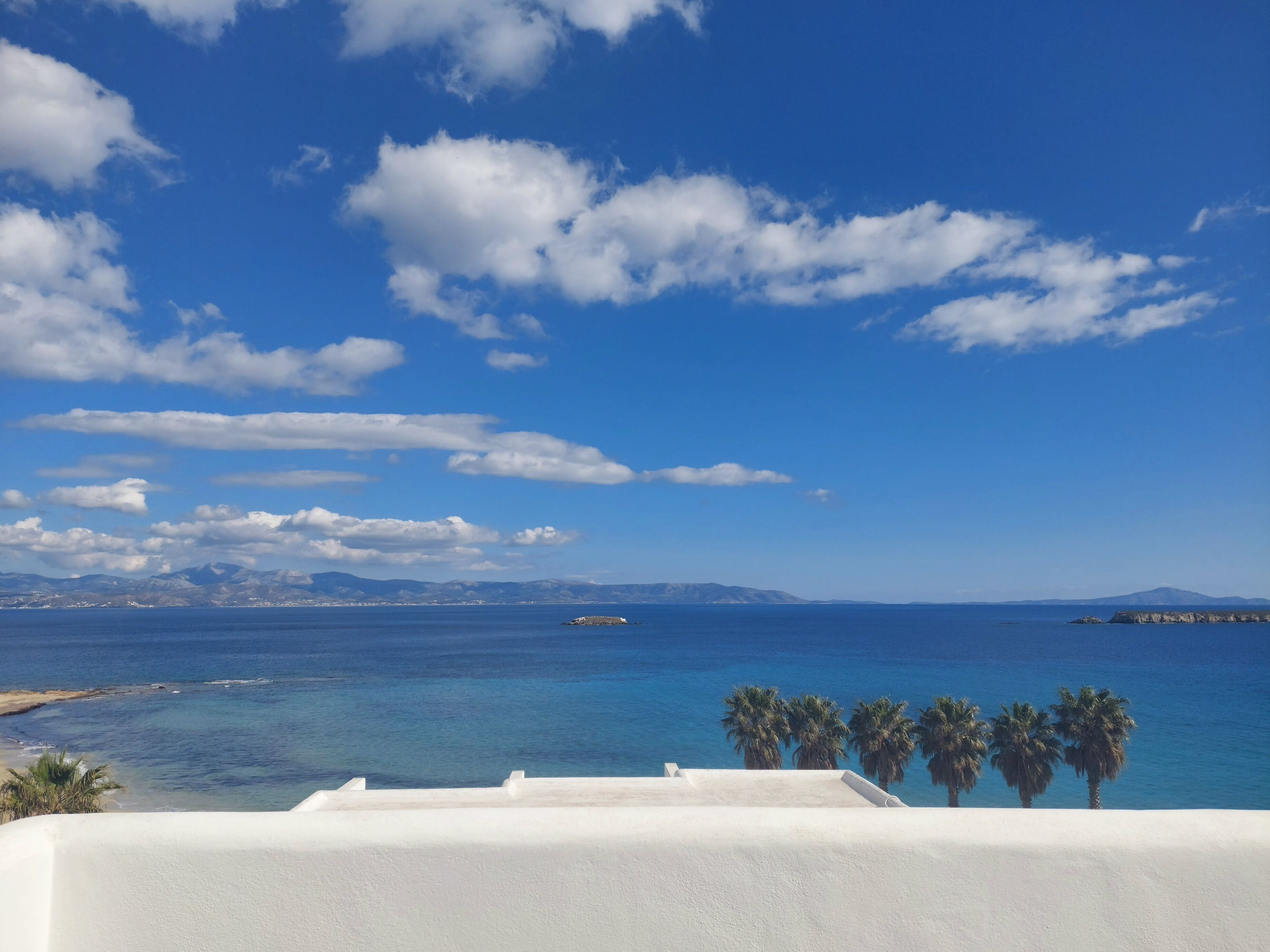 A coastal view with a clear sky, calm sea, and distant mountains.