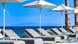 A poolside area with lounge chairs and umbrellas, overlooking a body of water and palm trees.