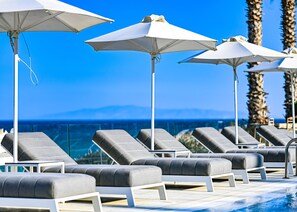 A poolside area with lounge chairs and umbrellas, overlooking a body of water and palm trees.