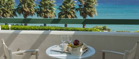 Ein Balkon mit Korbstühlen, einem Tisch mit Obstschale und zwei Gläsern, und Blick auf das Meer und Palmen.