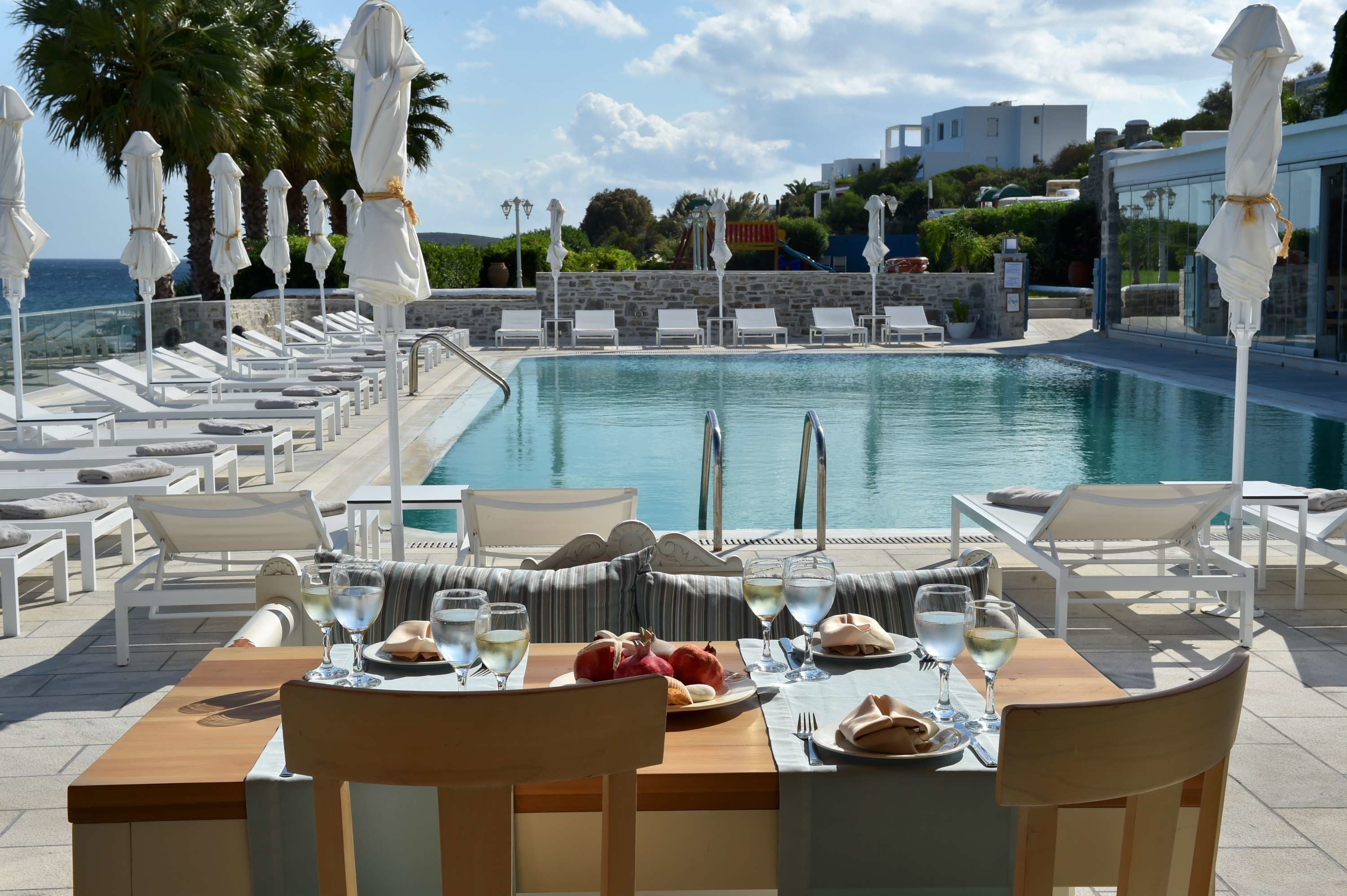 A poolside dining area with white lounge chairs, a pool, and umbrellas.