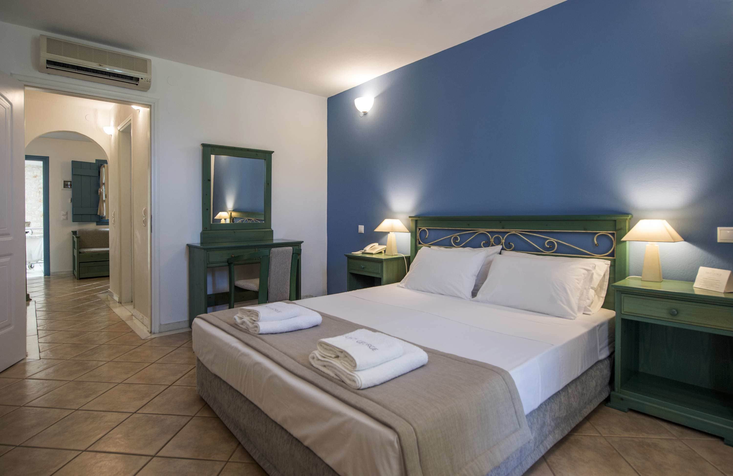 Une chambre d’hôtel comprenant un lit, deux tables de chevet avec des lampes, un bureau avec une chaise, un miroir et un appareil de climatisation.