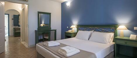 A hotel room with a bed, two bedside tables with lamps, a desk with a chair, a mirror, and an air conditioning unit.