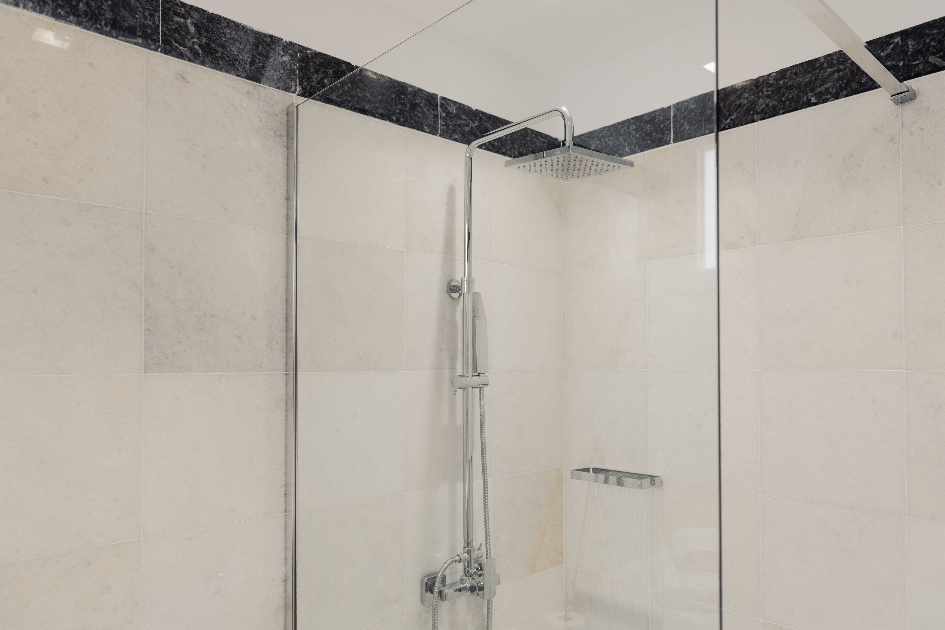 A modern shower with a glass enclosure, a handheld showerhead, and a wall-mounted control panel.
