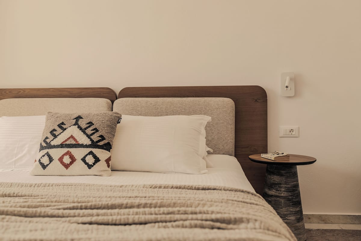 A bed with two pillows, a round side table, and a wall socket.