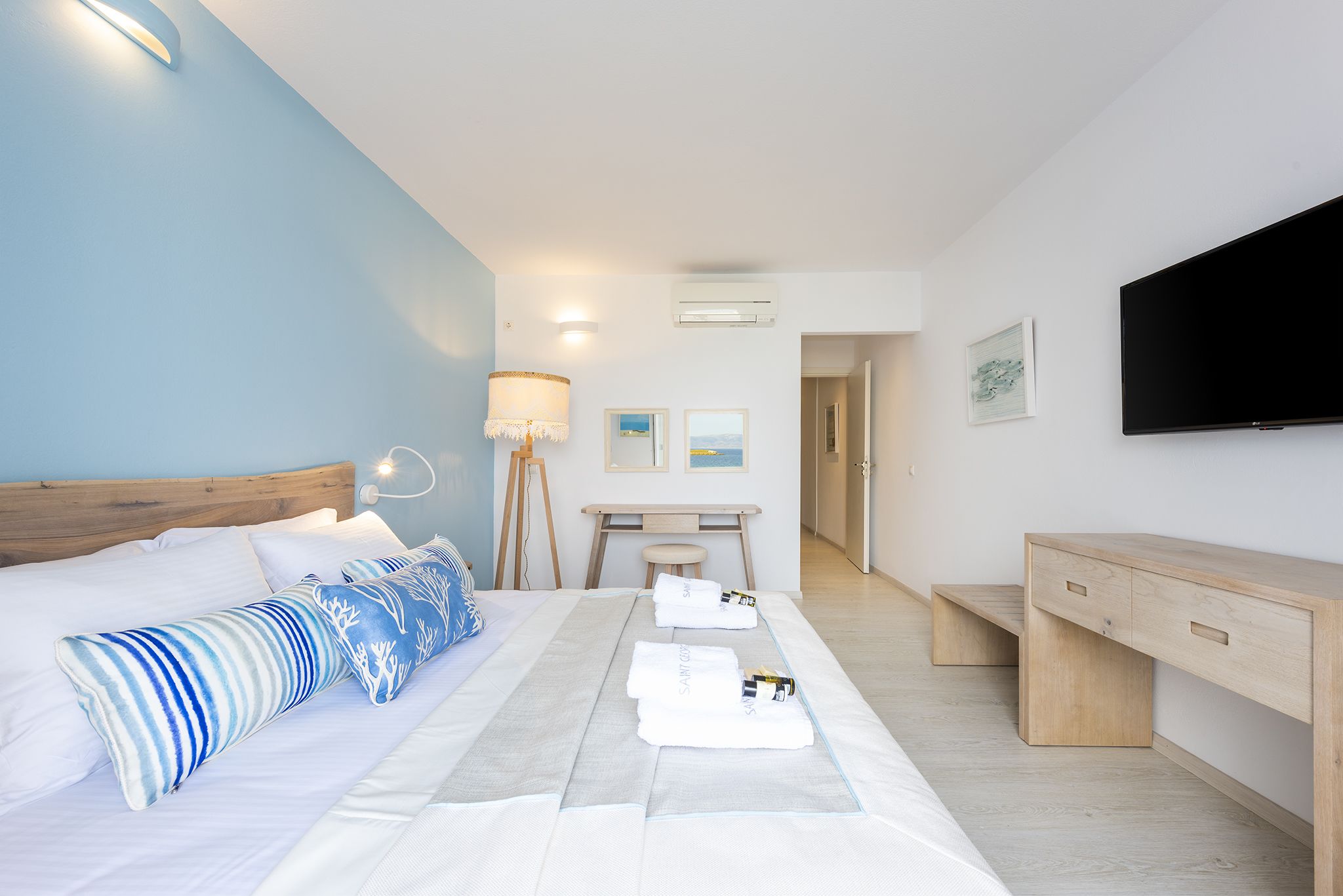 Habitación de hotel moderna con cama, escritorio, televisión y vista al pasillo.