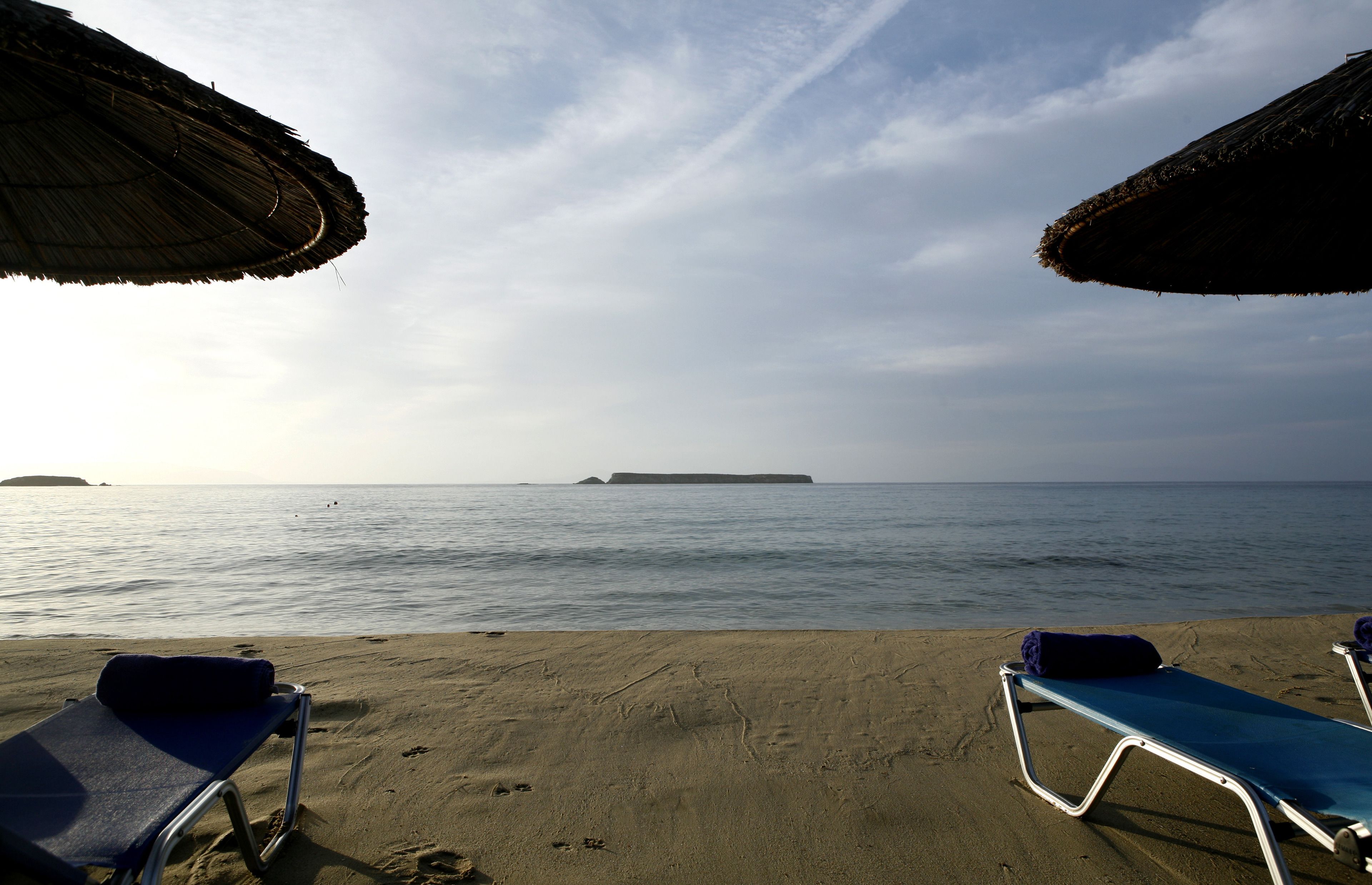 A beach with two sun loungers and a thatched umbrella.