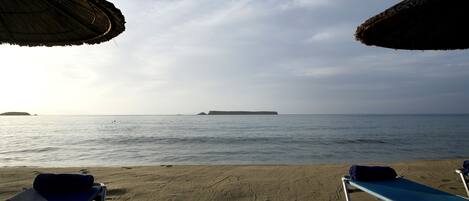 A beach with two sun loungers and a thatched umbrella.