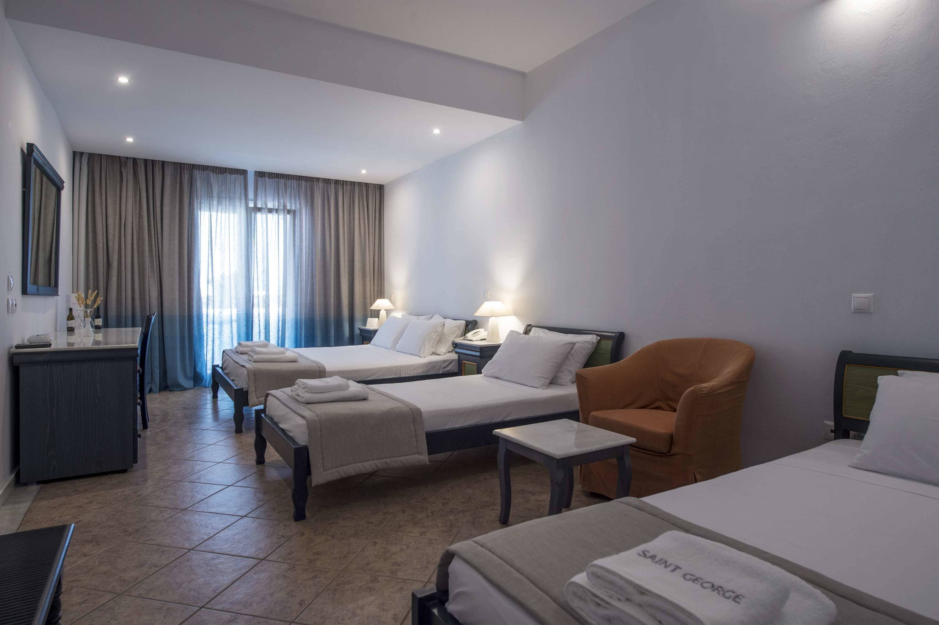 A hotel room with two beds, a desk, a chair, and a small table.