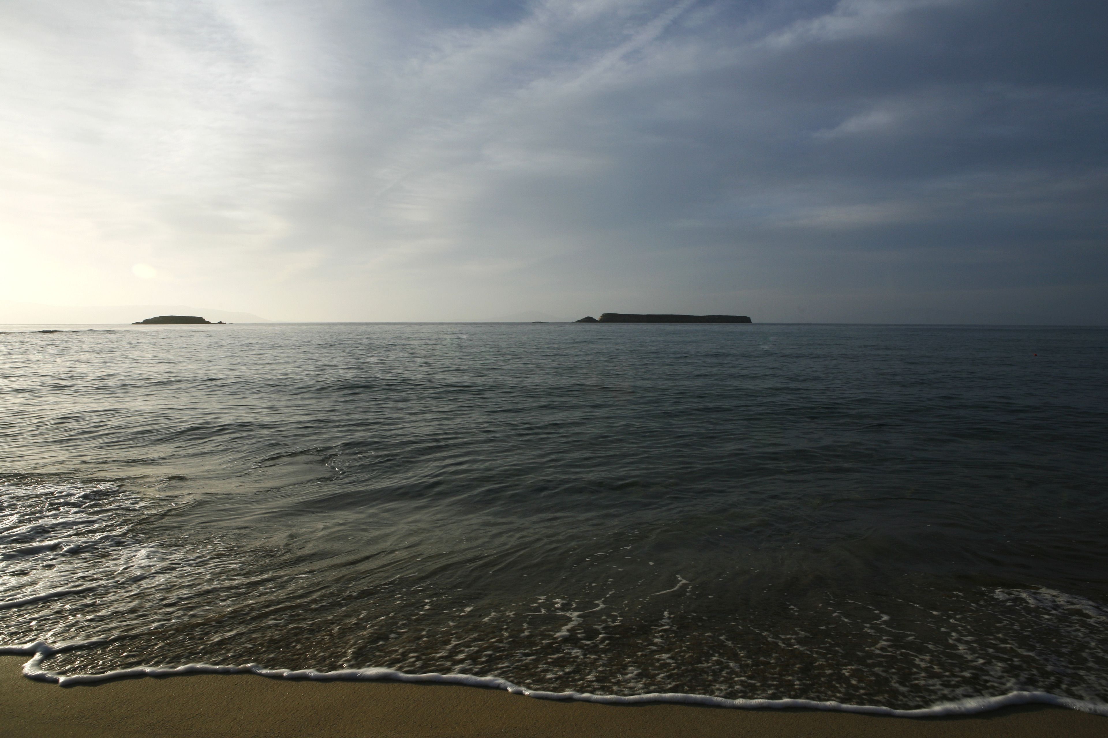 A beach with calm waters and distant landforms.