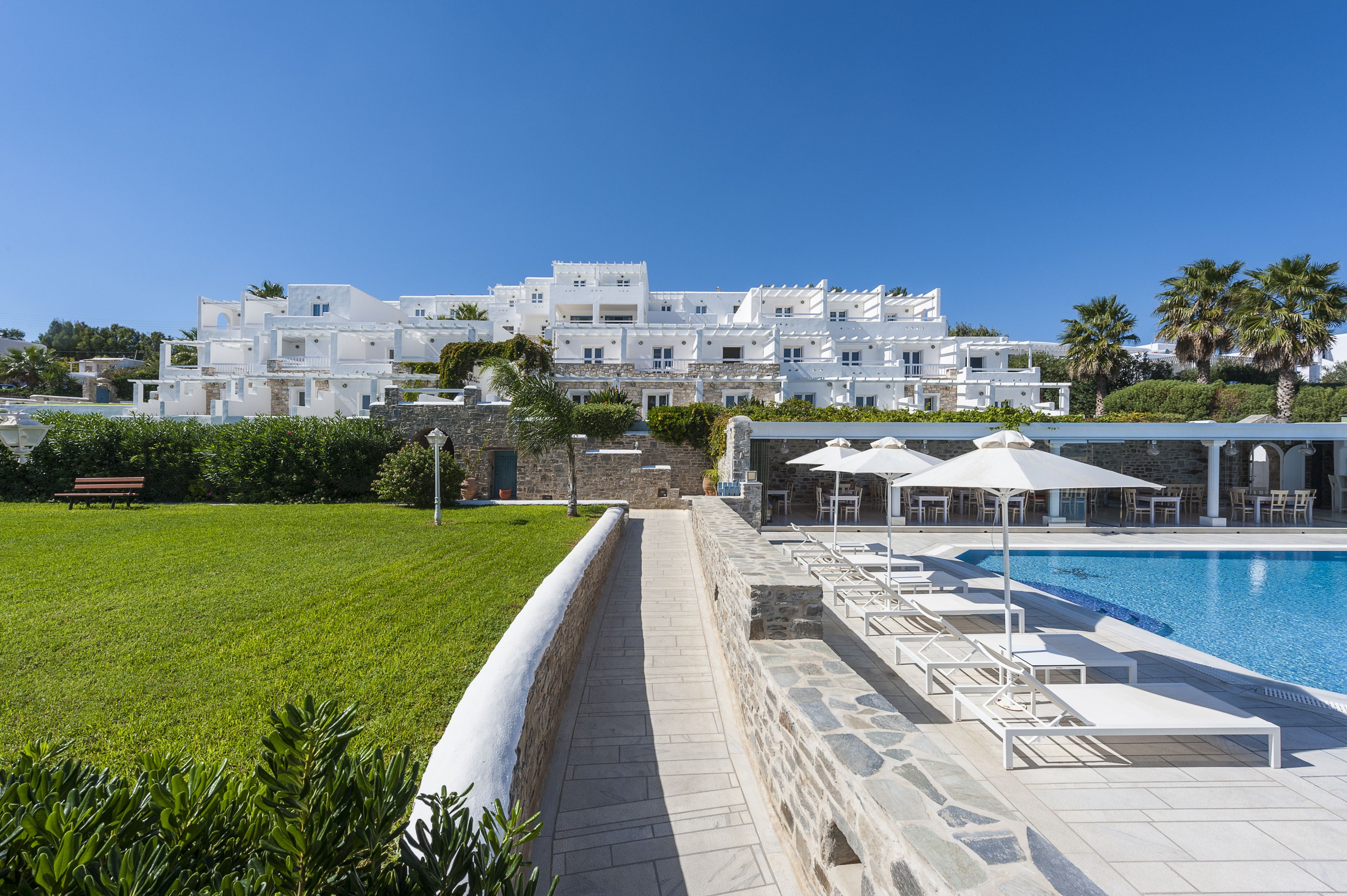 A pool area with lounge chairs and umbrellas, a stone pathway, and a white building in the background.