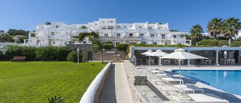 A pool area with lounge chairs and umbrellas, a stone pathway, and a white building in the background.