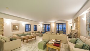 A spacious living room with multiple sofas, a wooden coffee table, and large windows offering a view of the outdoors.