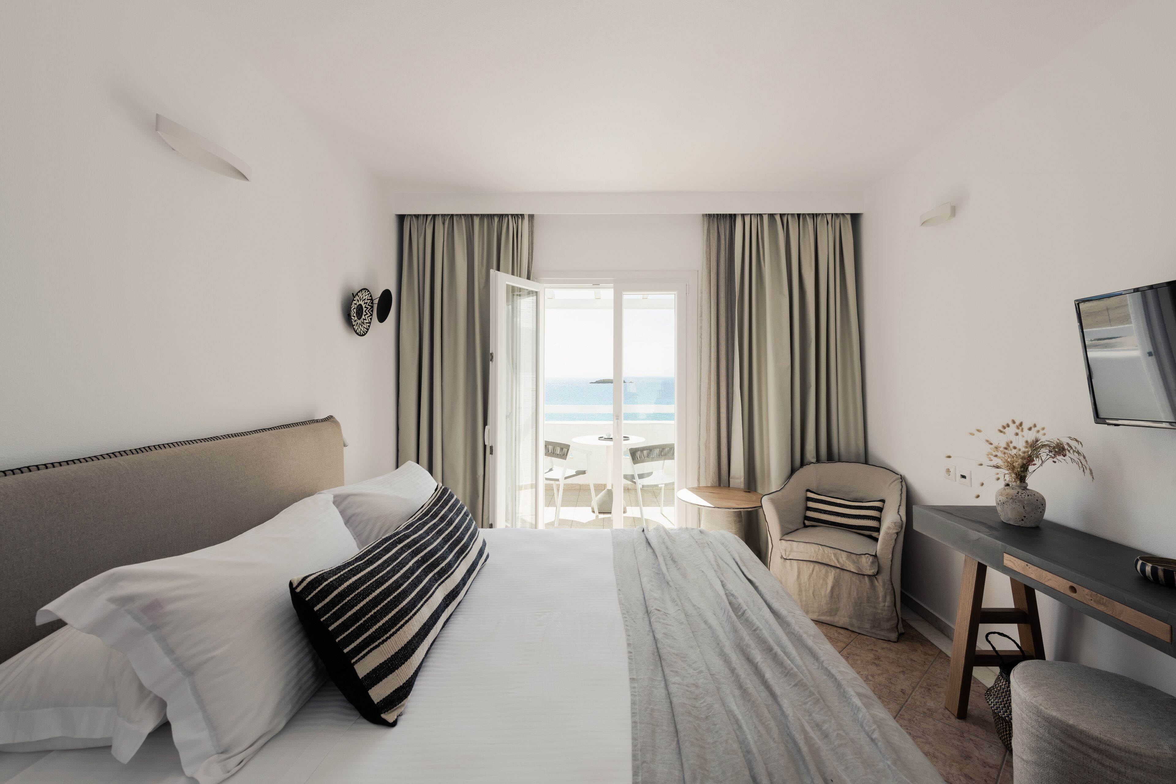 A hotel room with a bed, a desk, a chair, and a view of the sea.