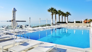 A pool area with white lounge chairs and umbrellas, palm trees, and a clear view of the sea. - Saint George Hotel (Paros)