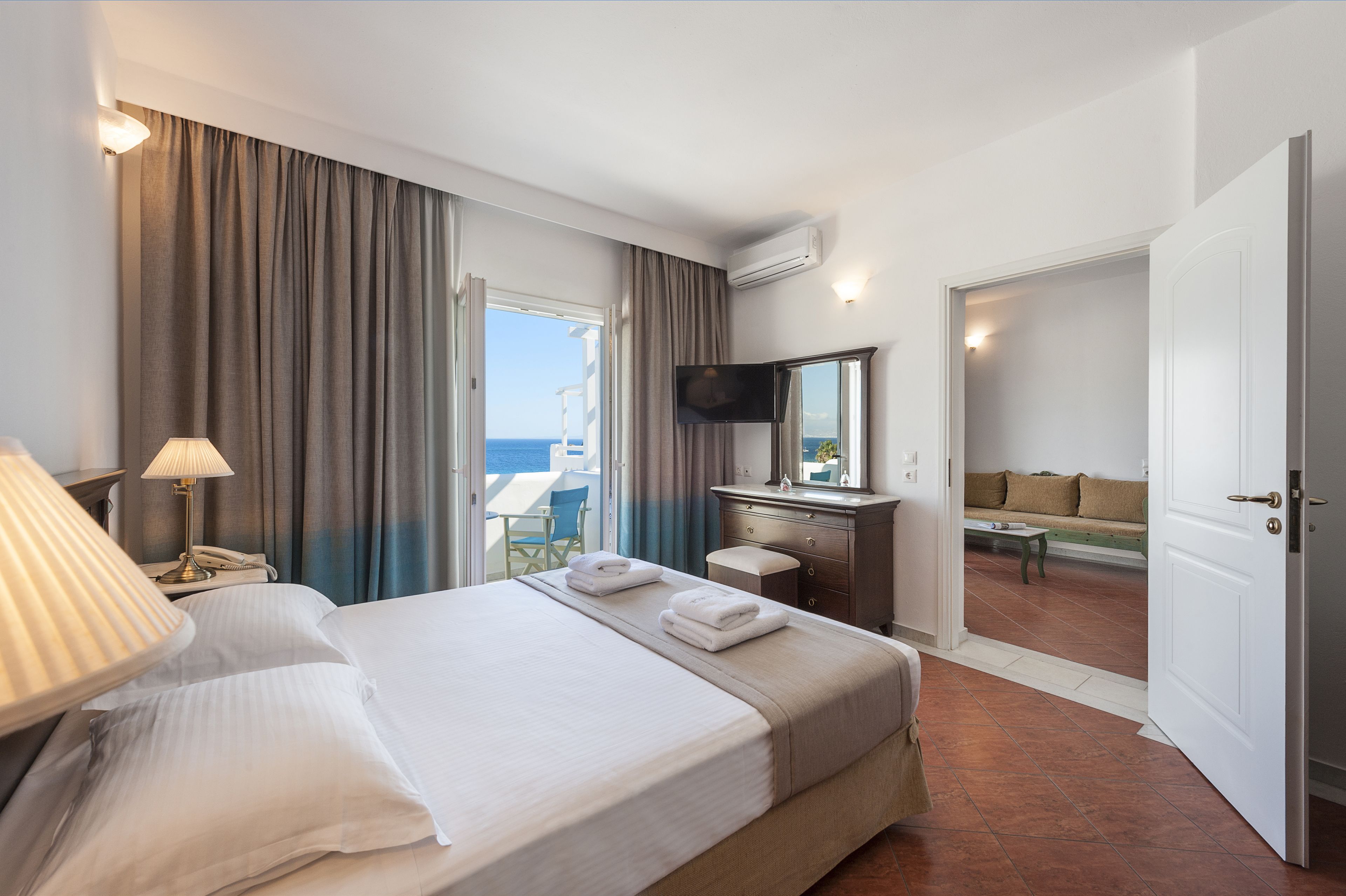 Quarto de hotel com cama, escrivaninha, televisão e vista para o mar.