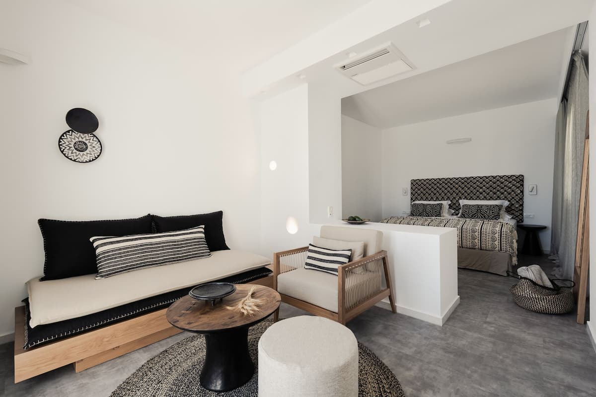 A modern, minimalist bedroom with a bed, bedside table, and a small seating area.