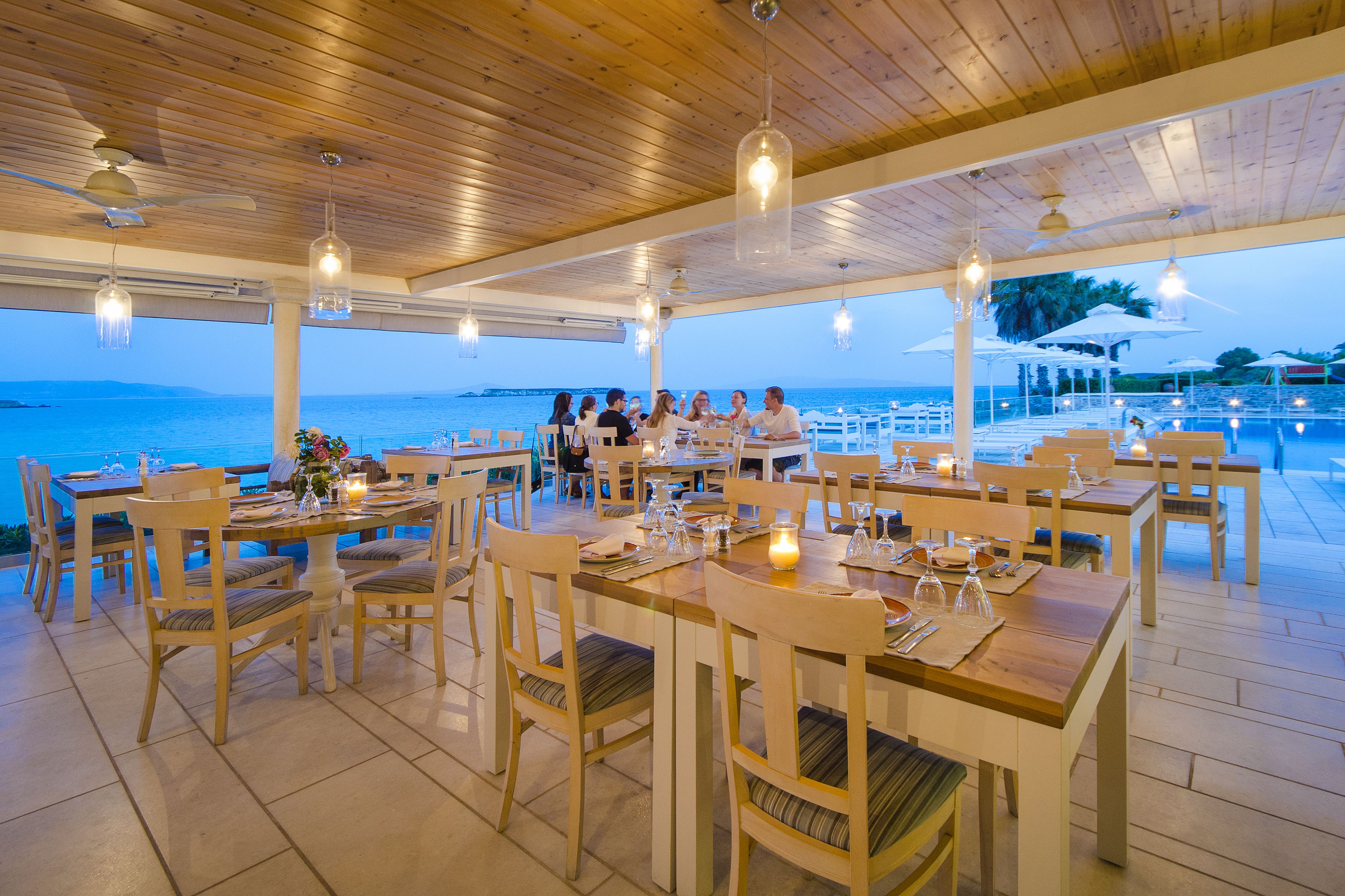 Un área de comedor al aire libre con mesas y sillas de madera, con vista al mar.