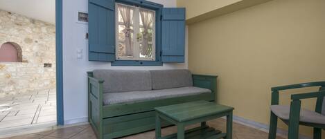 Quarto com sofá verde, mesa do mesmo tom e janela com persianas azuis.