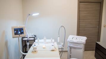 A medical examination room with a treatment bed, a monitor, a sink, and a waste bin.