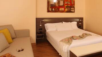 A hotel room with a bed, a sofa, a nightstand, and a painting on the wall.
