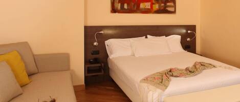 A hotel room with a bed, a sofa, a nightstand, and a painting on the wall.