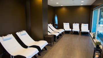 Relax in a serene spa room with reclining chairs, a wooden stool, and a potted plant.
