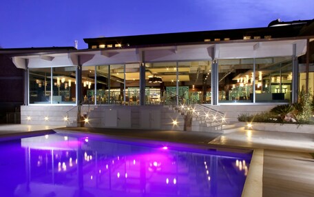 A modern building with a glass facade, a pool with purple lighting, and a staircase leading to the upper levels.