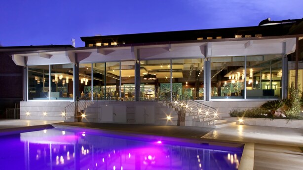 A modern building with a glass facade, a pool with purple lighting, and a staircase leading to the upper levels. - Hotel & Spa Villa Mercede (Frascati)