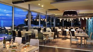 A modern dining area with tables set for dinner, large windows offering a view of the cityscape, and a contemporary interior design. - Hotel & Spa Villa Mercede (Frascati)