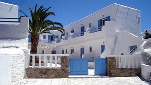A white building with blue doors and windows, a palm tree, and a stone wall. - Magas Hotel (Mykonos)