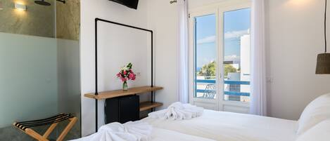 Habitación de hotel con dos camas, ducha, televisor, pequeño escritorio con un jarrón de flores y balcón con vistas.