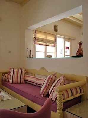 A living room with a sofa, a chair, and a mirror reflecting a window with curtains. - Magas Hotel (Mykonos)