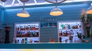 A bar area with shelves of bottles, hanging lights, and bar stools. - Magas Hotel (Mykonos)