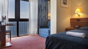 A hotel room with a bed, a chair, a desk, and a view of the sea through large windows. - Hotel Kristal - Liburnia (Opatija)