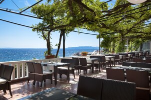 An outdoor dining area with tables and chairs, overlooking the sea.