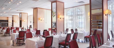 Un comedor amplio con varias mesas y sillas, ventanas grandes y lámparas fijadas a la pared.