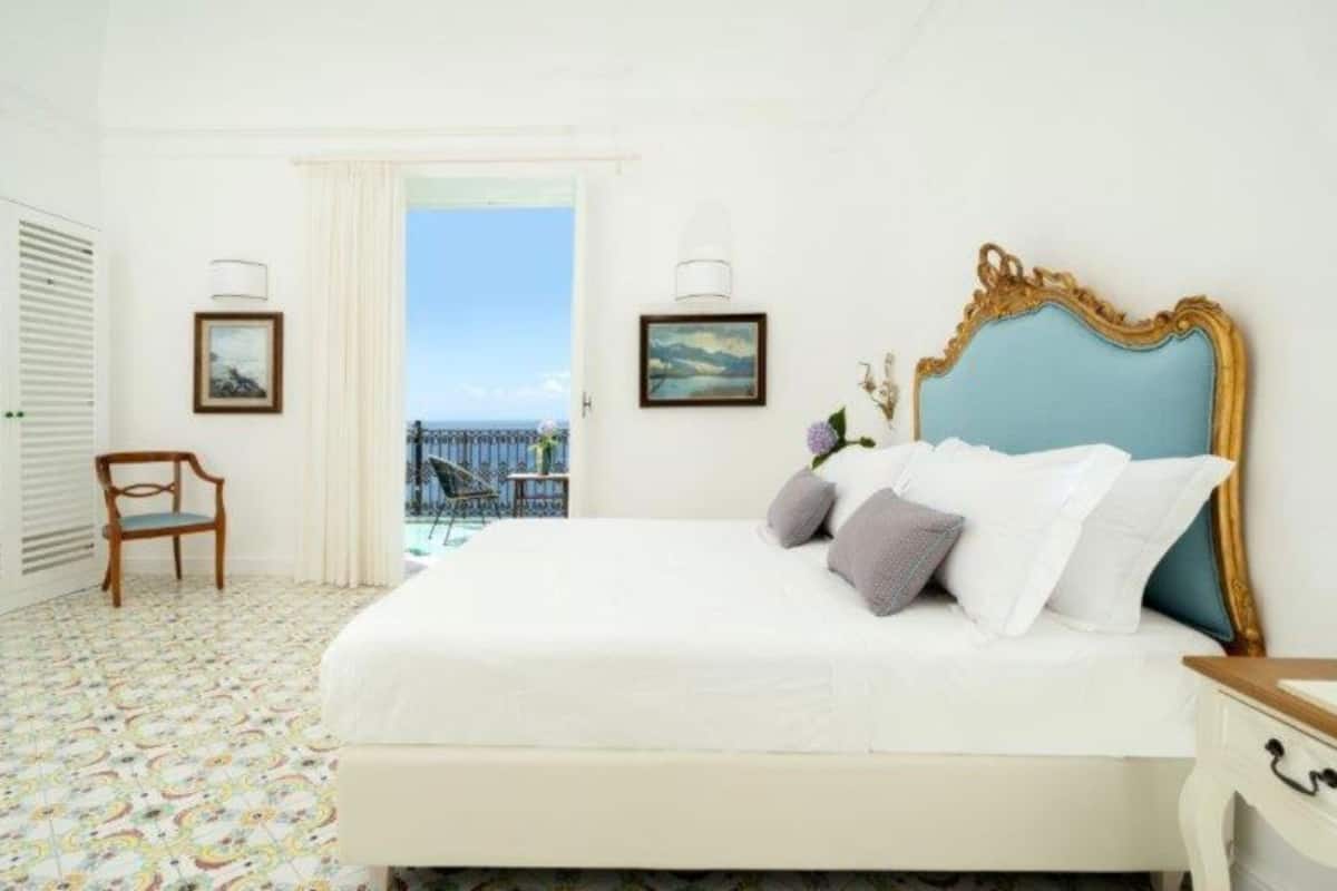 A bedroom with a bed, a chair, a nightstand, and a view of the sea.