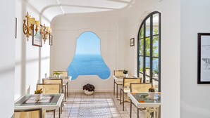 A dining area with a view of the sea, featuring a white interior, tiled floor, and modern furniture.