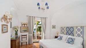 A bedroom with a large bed, a wooden dresser, a chair, a chandelier, and a view of the outdoors.
