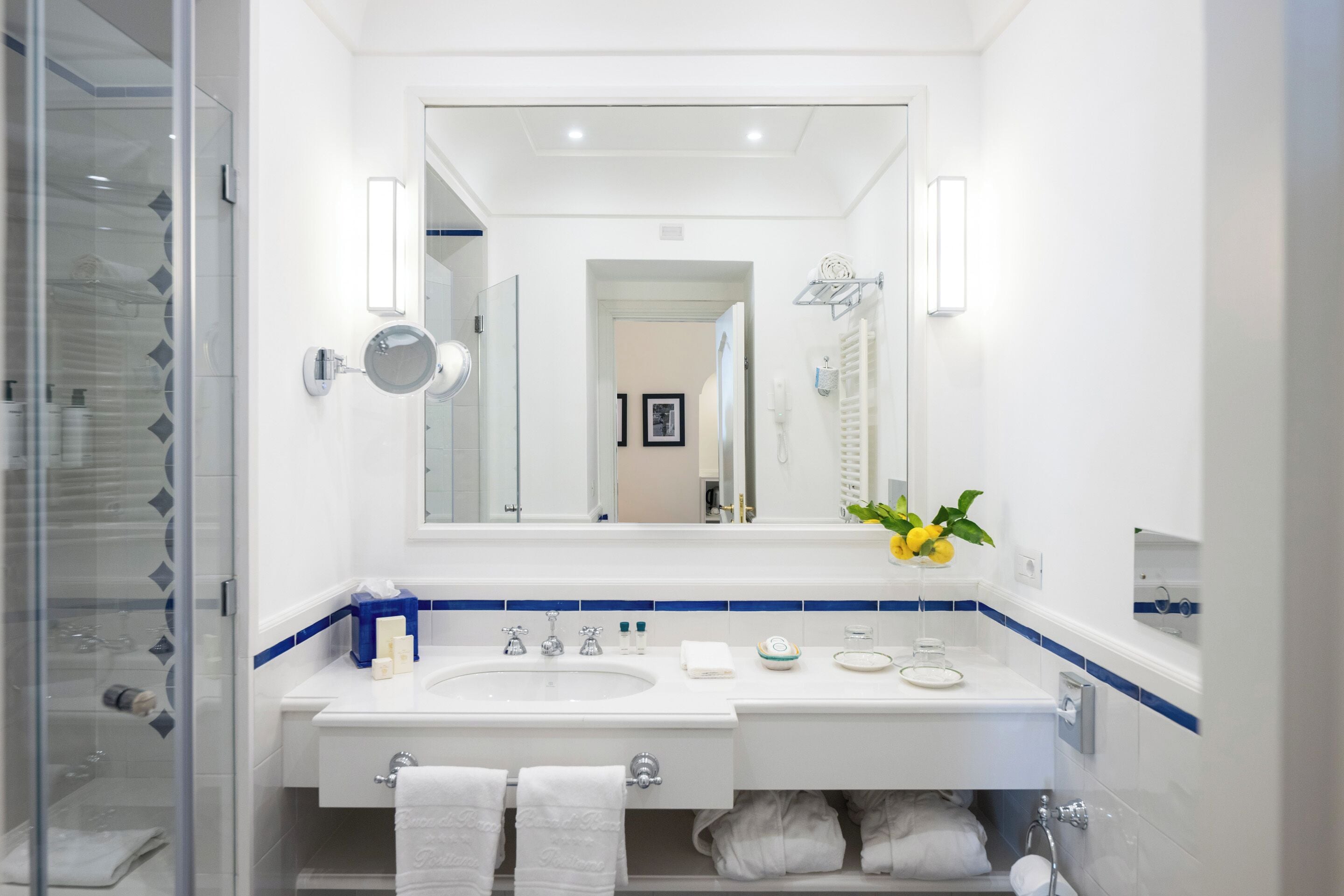 Een moderne badkamer met een grote spiegel, twee wasbakken, een douchecabine met glazen wanden en een handdoekrek.