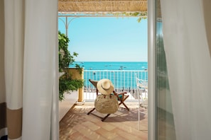 A balcony with a view of the sea, a wicker chair, and a potted plant. - Hotel Buca di Bacco (Positano)