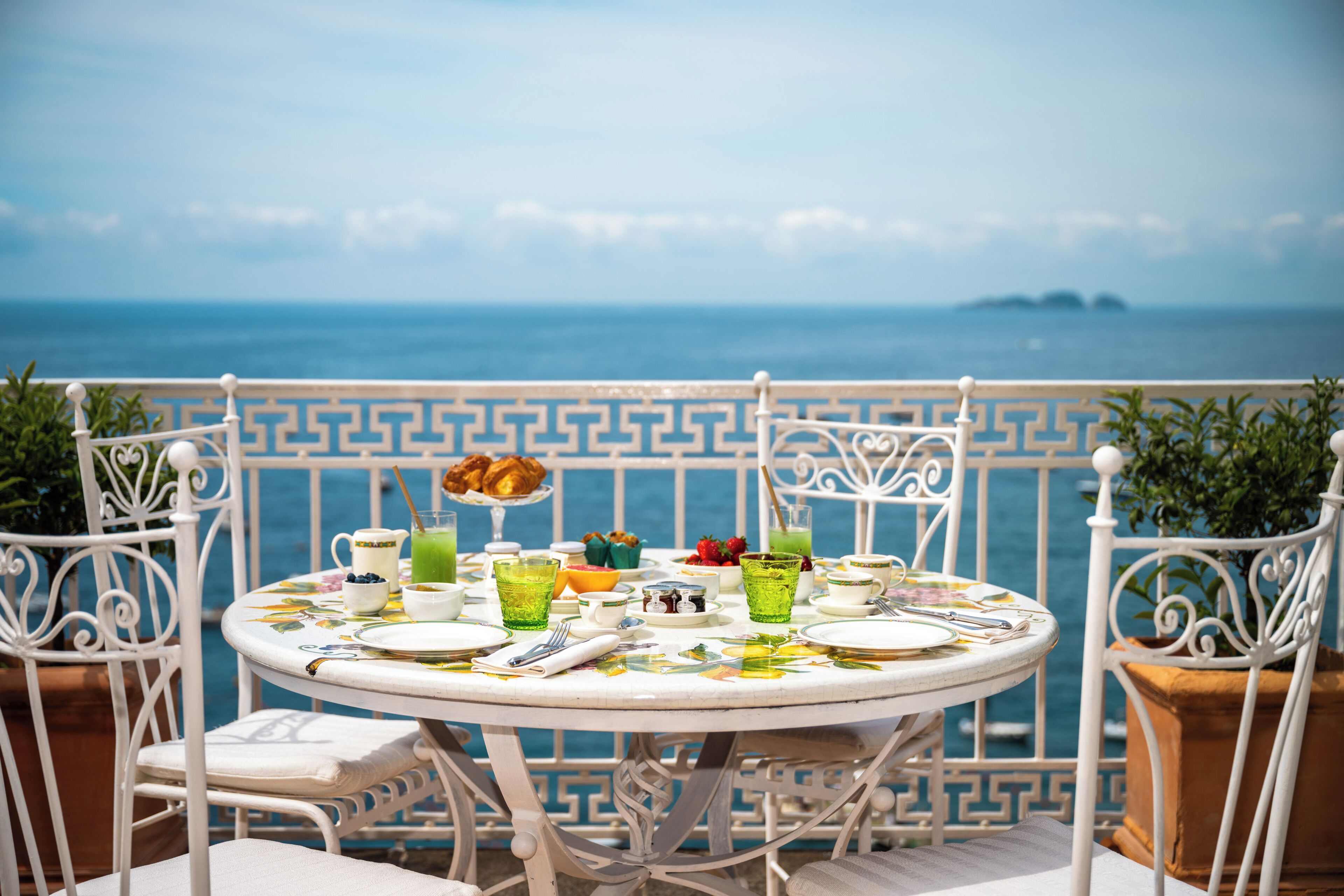 Mesa redonda con vistas al mar, dispuesta con platos, tazas y una bebida verde.