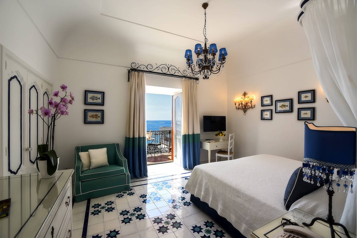 Habitación de hotel con cama, escritorio, silla, televisión y balcón con vistas al mar.